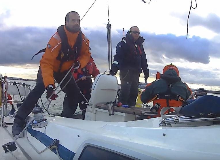 pass RYA practical exam first time — three people in sailing gear maneuvering a boat under cloudy sky