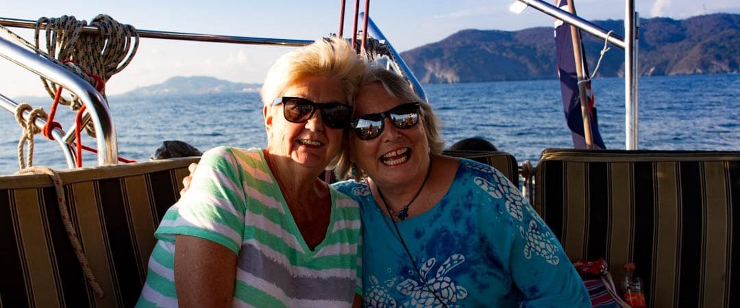 pass RYA practical exam first time — two people smiling on a boat with ocean and mountains behind