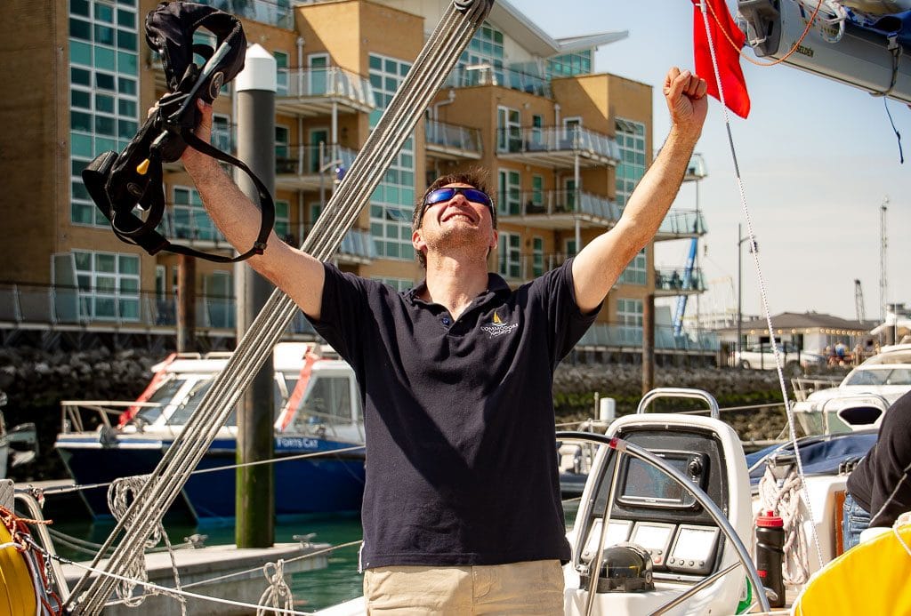 learning to sail at 40 — person joyfully raising arms on a sailboat wearing sunglasses