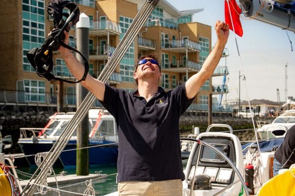 pass RYA practical exam first time — person on a sailboat celebrating near a marina with modern buildings
