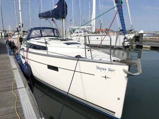 A sailboat named "Mayan Star" is docked at a marina, surrounded by other boats, with clear skies and calm water.
