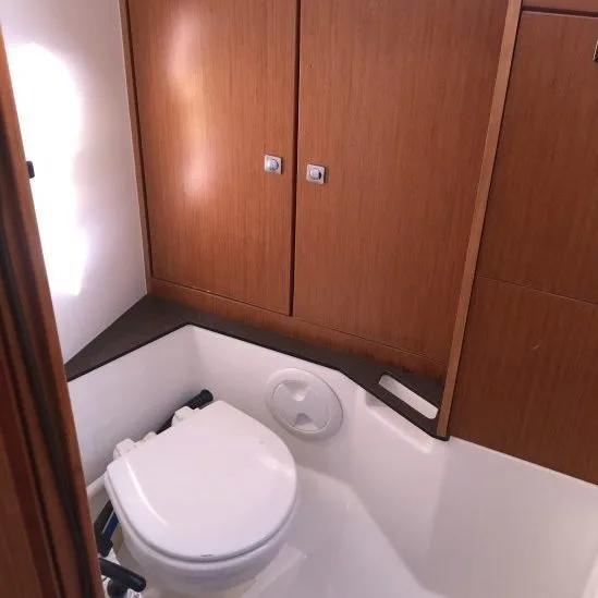 Compact restroom with a white toilet and wooden cabinets on a boat, featuring a minimalistic design and storage space.