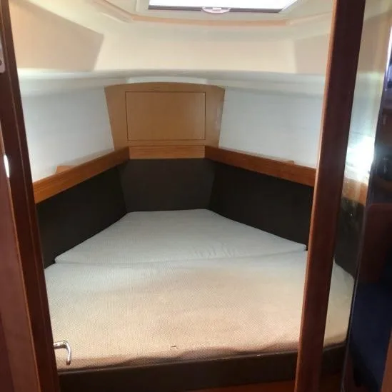 Cozy boat cabin with a cushioned bed, wooden paneling, and a small overhead window, creating a compact and comfortable living space.