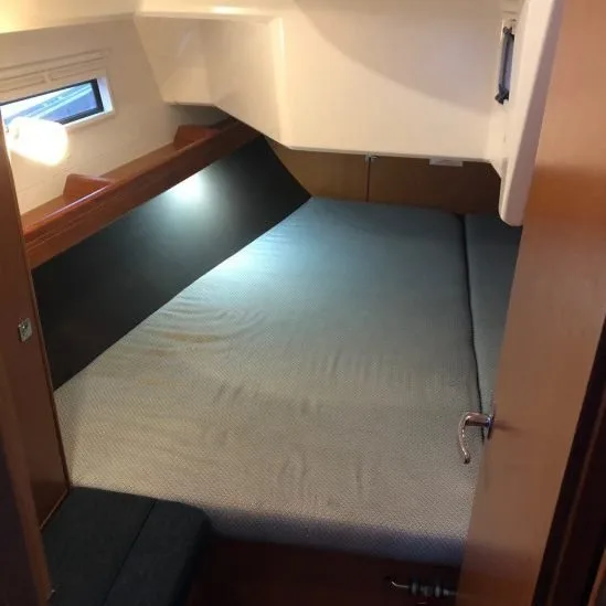 Compact sleeping quarters with a fitted bed, wooden walls, small window, and overhead lighting, creating a cozy and efficient space.