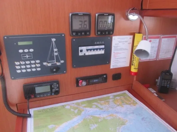 A boat's navigation station features control panels, communication equipment, and a marine map, possibly the Isle of Wight, displayed on a wooden desk.