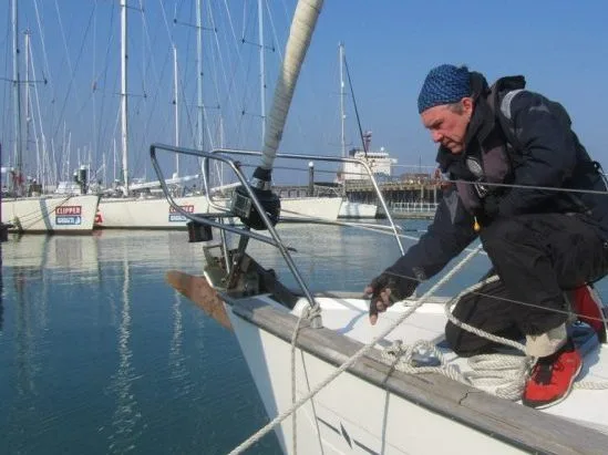 A person secured ropes on a boat in a marina, surrounded by other sailboats under a clear blue sky.