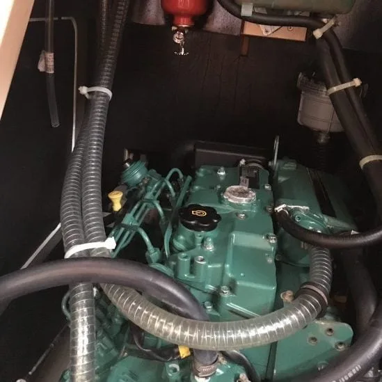The image shows a green engine inside a confined space with several hoses and cables attached around it. A red tank is visible above.