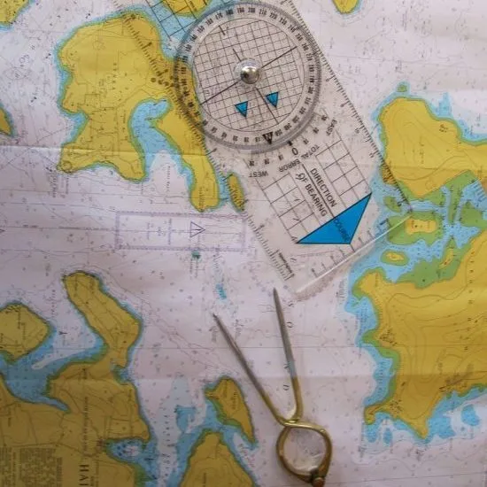A nautical chart with navigation tools, including a protractor and a pair of dividers, is used for plotting maritime courses.