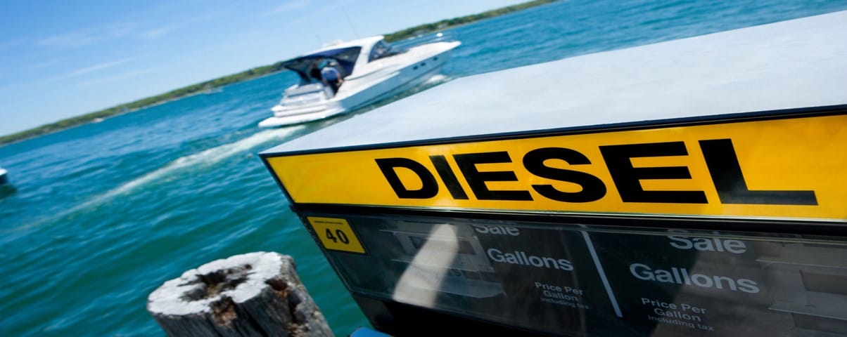 A boat on a lake near a pier with a diesel fuel pump in the foreground under a clear blue sky.